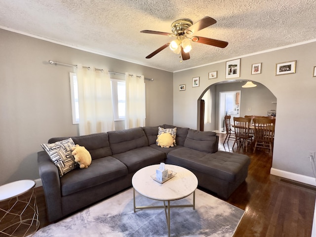 living room with arched walkways, ceiling fan, a textured ceiling, wood finished floors, and ornamental molding