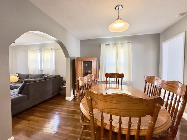 dining space with arched walkways and dark wood-type flooring