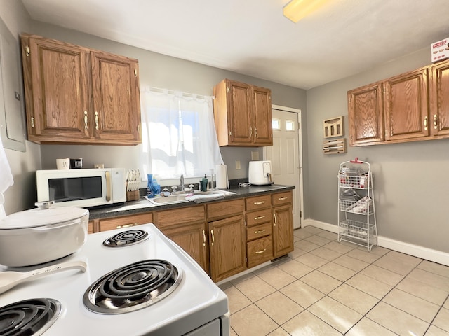 kitchen with white appliances, baseboards, brown cabinetry, a sink, and light tile patterned flooring