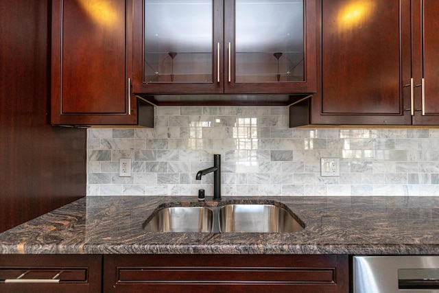 kitchen with glass insert cabinets, a sink, decorative backsplash, and dark stone countertops