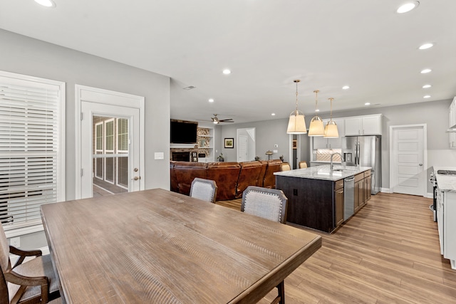 dining room with light wood-type flooring, ceiling fan, a fireplace, and recessed lighting