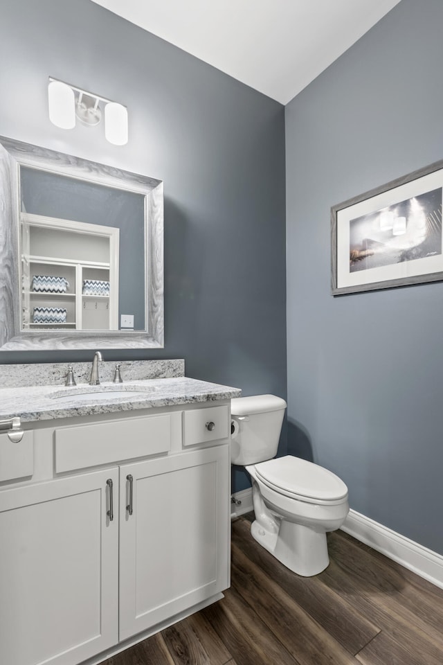 half bath featuring vanity, wood finished floors, toilet, and baseboards