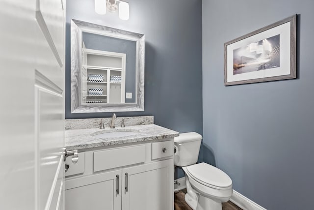 bathroom with toilet, wood finished floors, vanity, and baseboards