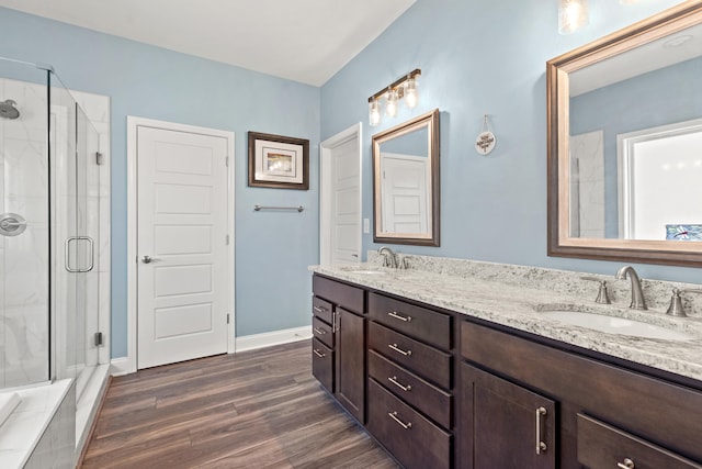 full bathroom featuring a stall shower, double vanity, a sink, and wood finished floors