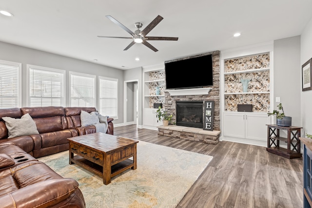 living area featuring built in features, light wood-style flooring, ceiling fan, a stone fireplace, and recessed lighting