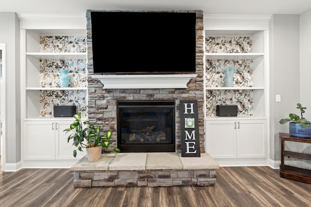 living area featuring dark wood-type flooring, built in shelves, a stone fireplace, and baseboards