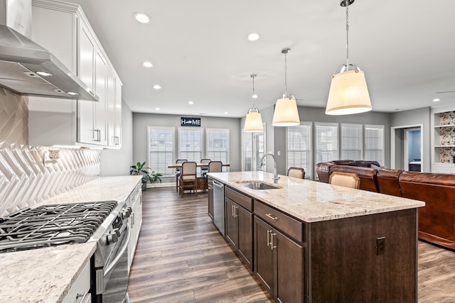 kitchen with wall chimney exhaust hood, hanging light fixtures, a sink, and stainless steel appliances