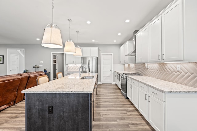 kitchen featuring pendant lighting, appliances with stainless steel finishes, open floor plan, a kitchen island with sink, and white cabinets