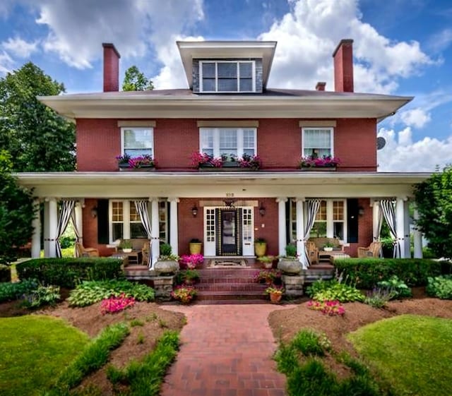 american foursquare style home with a porch, brick siding, and a chimney