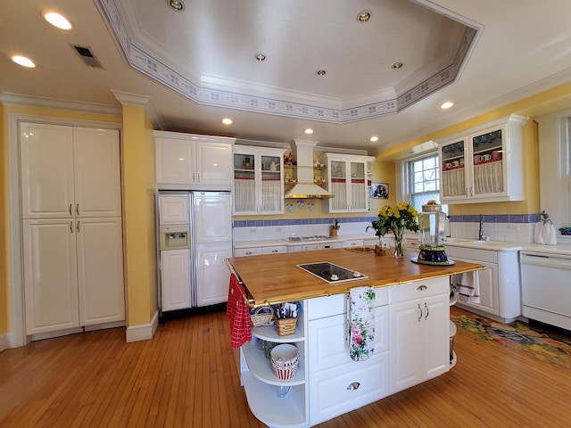 kitchen with glass insert cabinets, custom exhaust hood, a tray ceiling, white cabinetry, and wooden counters