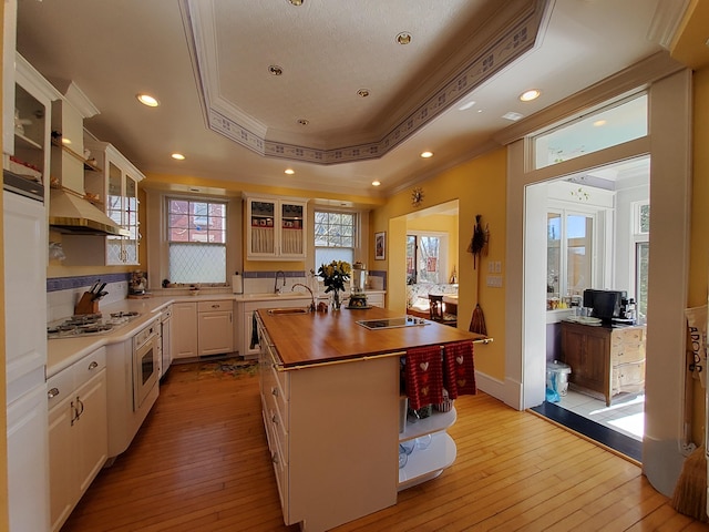 kitchen with glass insert cabinets, butcher block countertops, open shelves, a raised ceiling, and a center island with sink