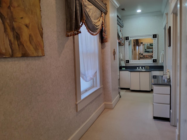 corridor with visible vents, baseboards, a sink, and ornamental molding