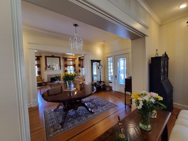 dining space featuring baseboards, wood finished floors, an inviting chandelier, crown molding, and a fireplace