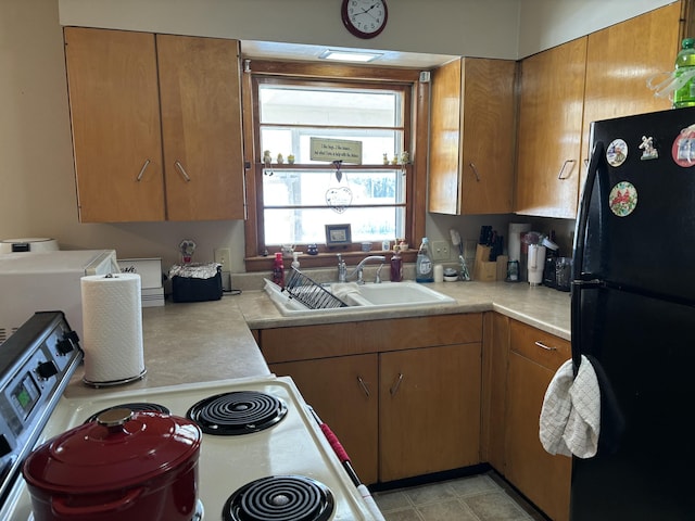 kitchen featuring a sink, light countertops, electric stove, freestanding refrigerator, and brown cabinetry