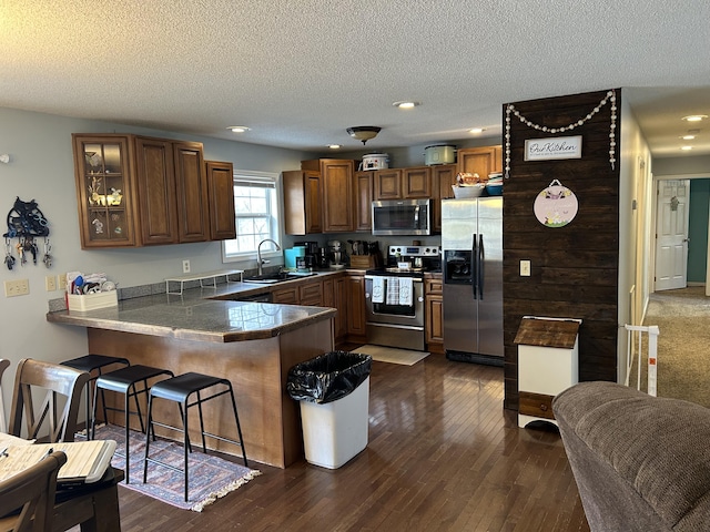 kitchen featuring appliances with stainless steel finishes, glass insert cabinets, dark wood-type flooring, a peninsula, and a sink