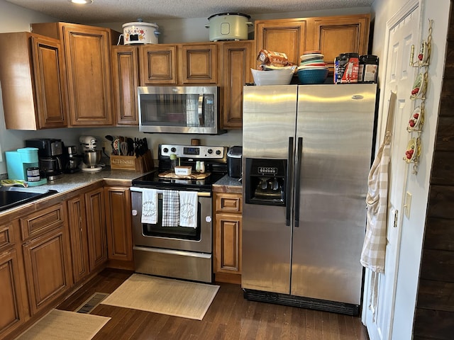 kitchen with visible vents, brown cabinetry, dark countertops, dark wood-style floors, and appliances with stainless steel finishes