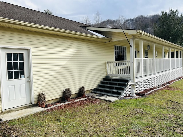 entrance to property featuring a shingled roof, a porch, and a lawn