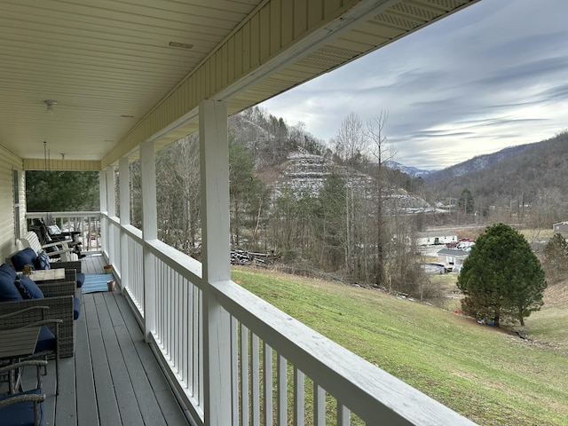 wooden terrace featuring covered porch, a lawn, and a mountain view