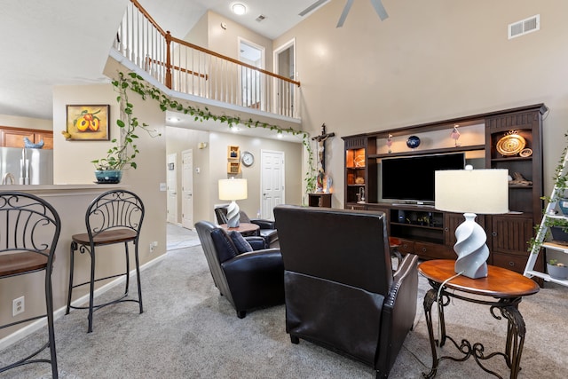 living area with light carpet, a ceiling fan, a towering ceiling, visible vents, and baseboards