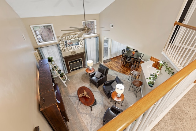 carpeted living room with ceiling fan, visible vents, vaulted ceiling, and a glass covered fireplace