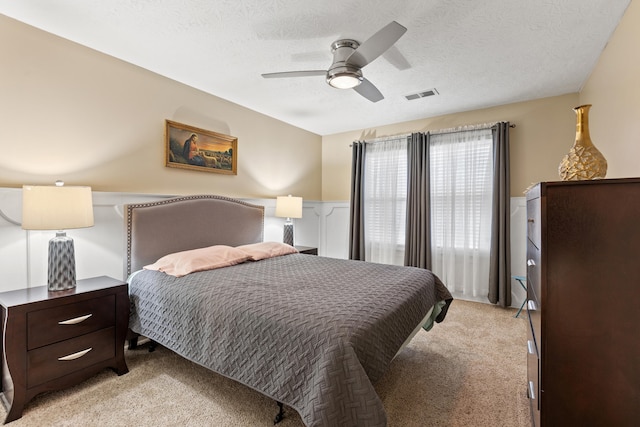 bedroom with light carpet, visible vents, a textured ceiling, and wainscoting