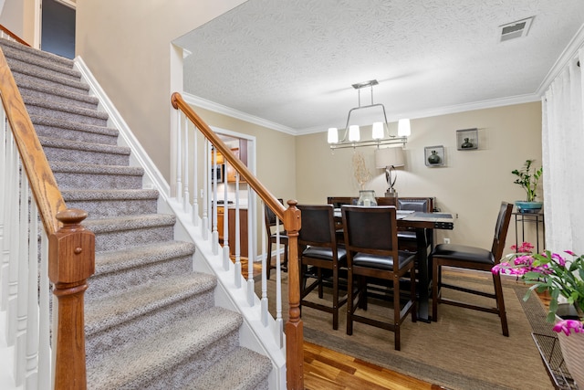 dining space featuring crown molding, visible vents, a textured ceiling, wood finished floors, and stairs