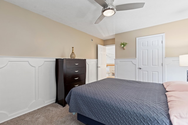 bedroom with a wainscoted wall, a decorative wall, a ceiling fan, and light colored carpet