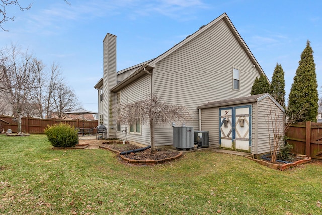 rear view of property featuring a yard, a chimney, a shed, a fenced backyard, and an outdoor structure