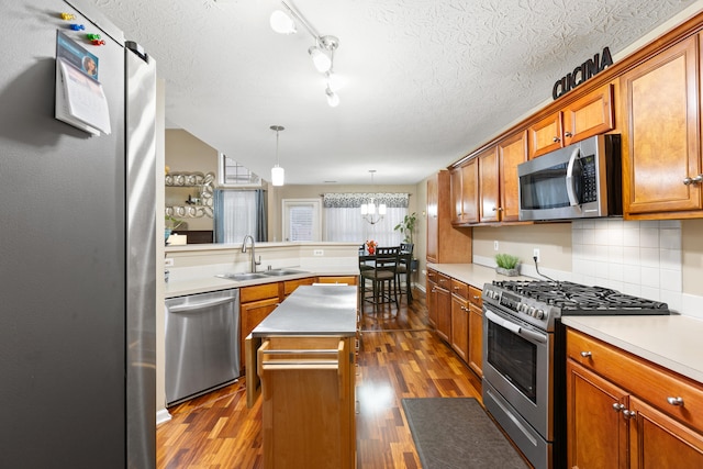 kitchen featuring brown cabinets, stainless steel appliances, hanging light fixtures, a kitchen island, and a sink