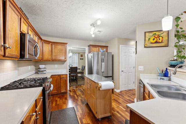 kitchen with a sink, light countertops, appliances with stainless steel finishes, hanging light fixtures, and brown cabinets