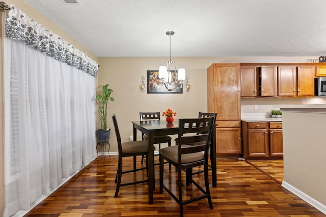 dining area featuring dark wood-style flooring, a textured ceiling, baseboards, and an inviting chandelier