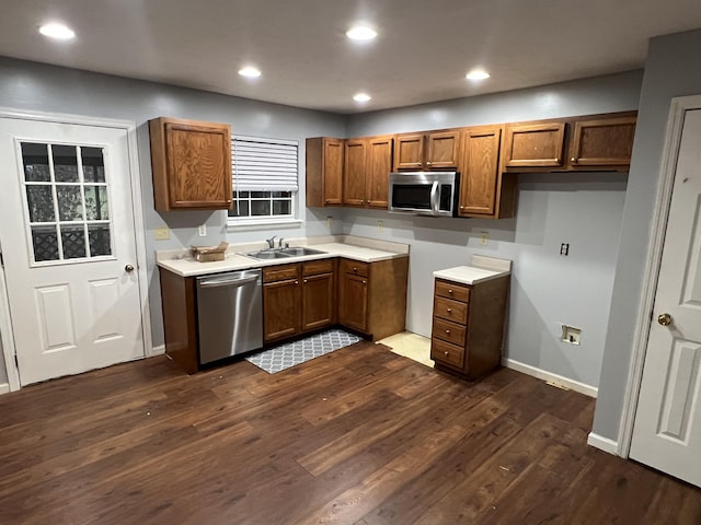 kitchen with brown cabinetry, dark wood-type flooring, stainless steel appliances, light countertops, and a sink