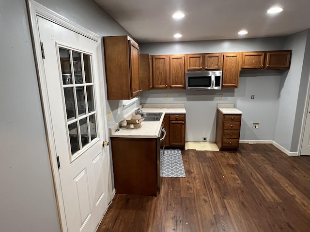 kitchen featuring dark wood-type flooring, a sink, light countertops, brown cabinets, and stainless steel microwave