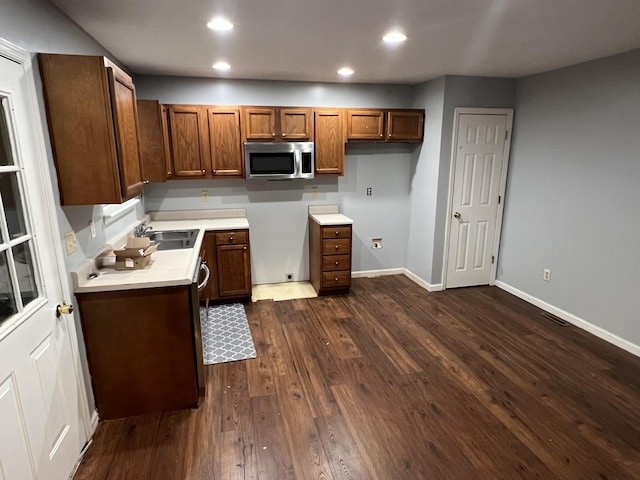 kitchen featuring dark wood-style flooring, a sink, light countertops, brown cabinetry, and stainless steel microwave