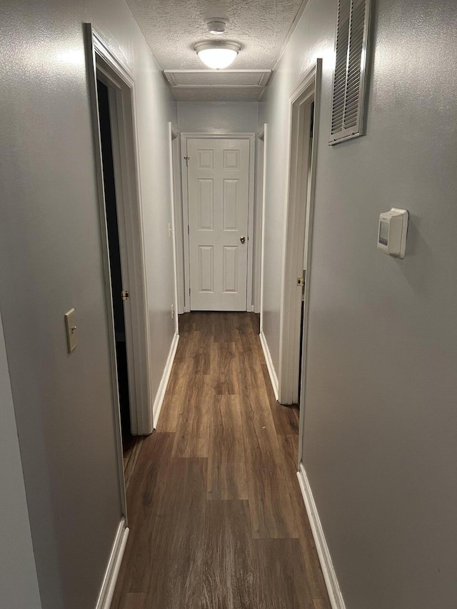 hall with baseboards, visible vents, dark wood finished floors, and a textured ceiling