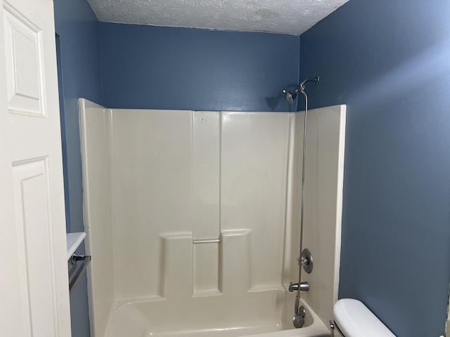 bathroom with a textured ceiling,  shower combination, and toilet