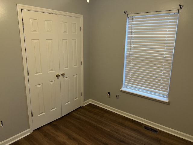 unfurnished bedroom featuring a closet, visible vents, dark wood finished floors, and baseboards