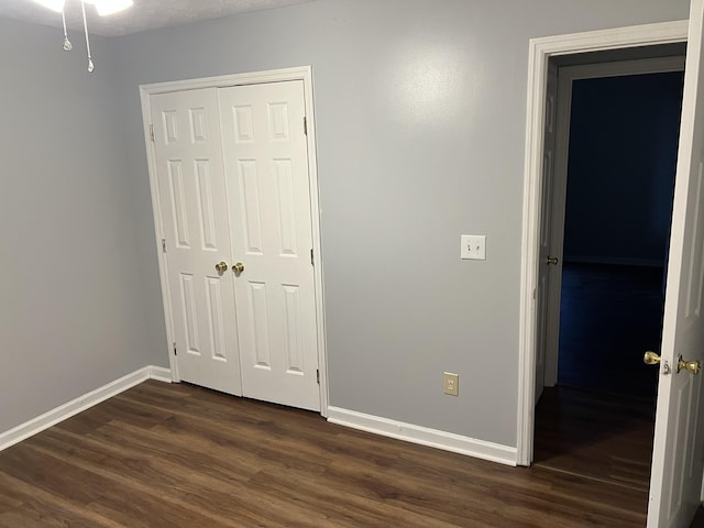 unfurnished bedroom with dark wood-type flooring, a closet, and baseboards