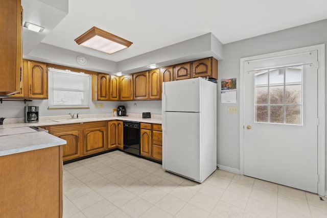 kitchen featuring a sink, black dishwasher, light countertops, freestanding refrigerator, and brown cabinetry