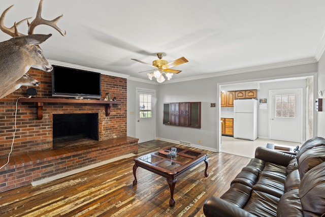 living room featuring a ceiling fan, baseboards, a brick fireplace, light wood-type flooring, and crown molding