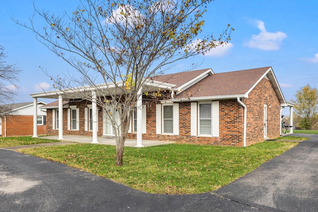 ranch-style house with roof with shingles, brick siding, and a front lawn