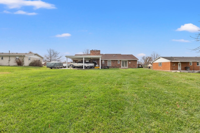 rear view of property featuring a yard, a carport, a chimney, and brick siding