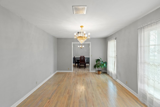 unfurnished dining area with a chandelier, light wood finished floors, and baseboards