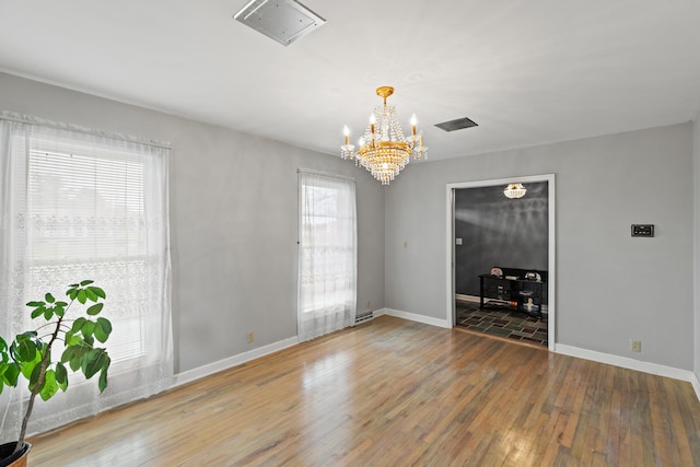 spare room with hardwood / wood-style flooring, baseboards, visible vents, and a chandelier