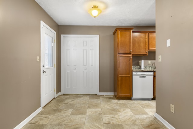 kitchen with brown cabinetry, white dishwasher, and baseboards