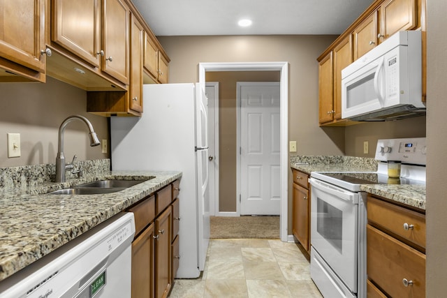 kitchen featuring white appliances, baseboards, brown cabinetry, light stone countertops, and a sink