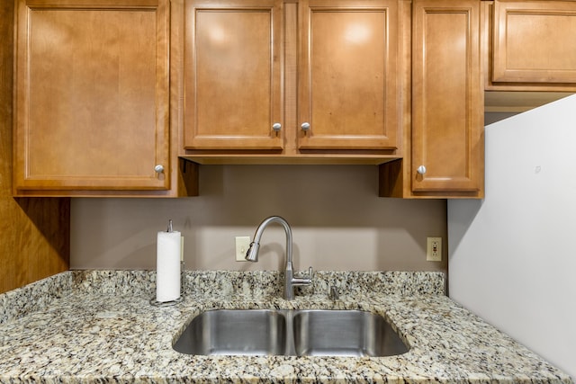 interior details featuring light stone counters, a sink, and brown cabinets