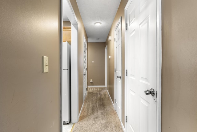 hall with light carpet, a textured ceiling, and baseboards