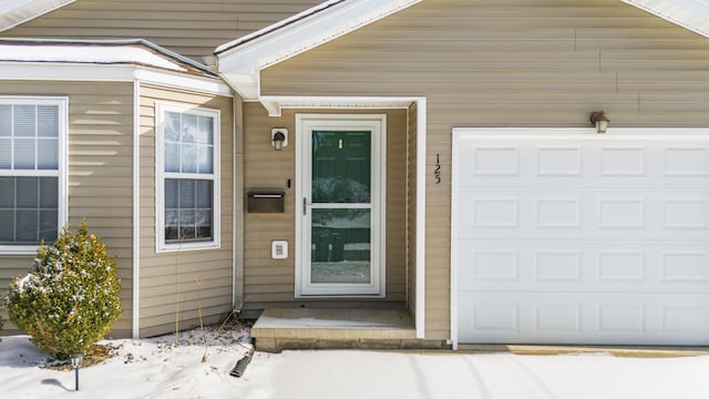 snow covered property entrance featuring a garage