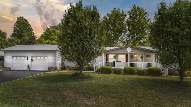 single story home with aphalt driveway, covered porch, a yard, and an attached garage